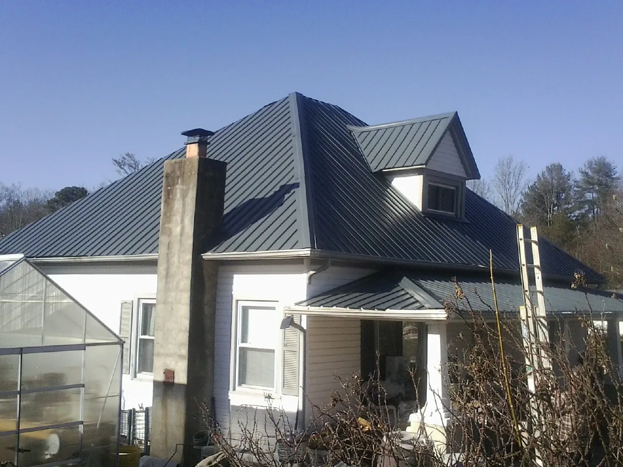 Dark blue standing seam metal roof on a white farmhouse with dormer — Slate & Tile Roof Repair by Roofing Brothers in Marble Falls