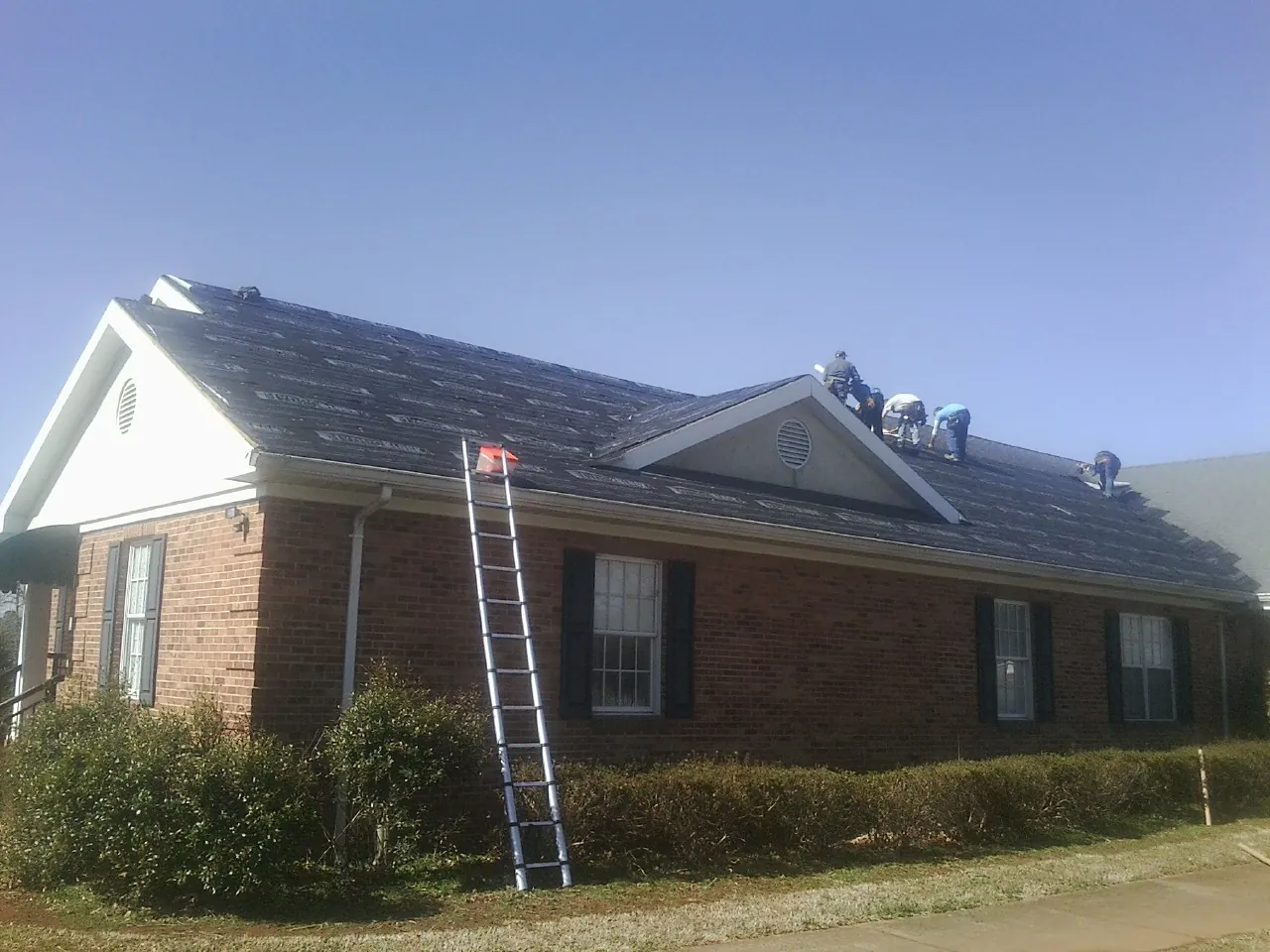 Crew tearing shingles off a brick ranch roof with a ladder set — Emergency Roof Repair work by our crew in Marble Falls