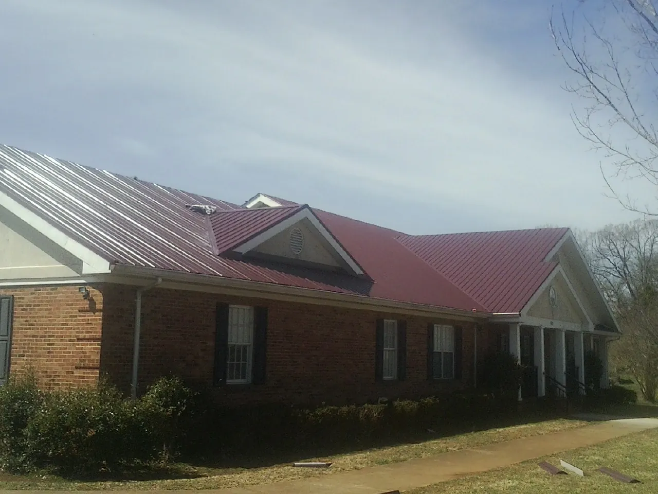Red metal roof with gabled entries on a long brick building, from a Hail Damage Roof Repair job in Marble Falls