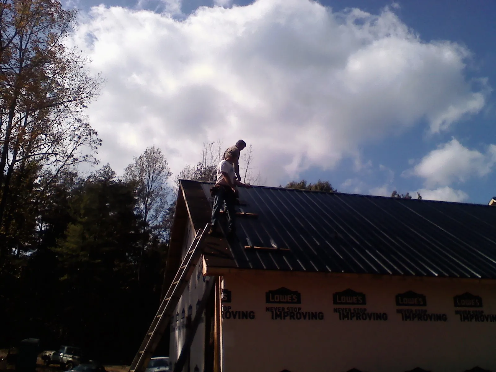 Roofer fastening dark metal panels high against a cloudy sky, from a Roof Inspection job in Marble Falls